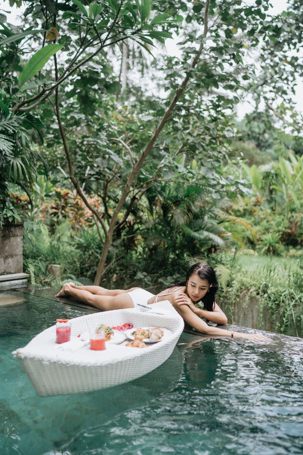 Floating breakfast tray with fresh food and drinks in an infinity pool with jungle views.