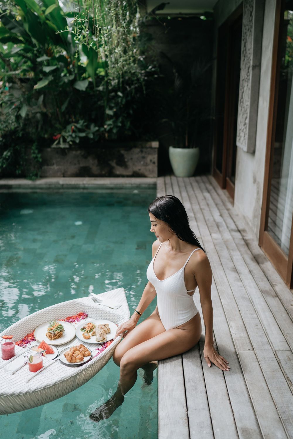 Woman enjoying poolside breakfast at a luxury villa with tropical garden views.
