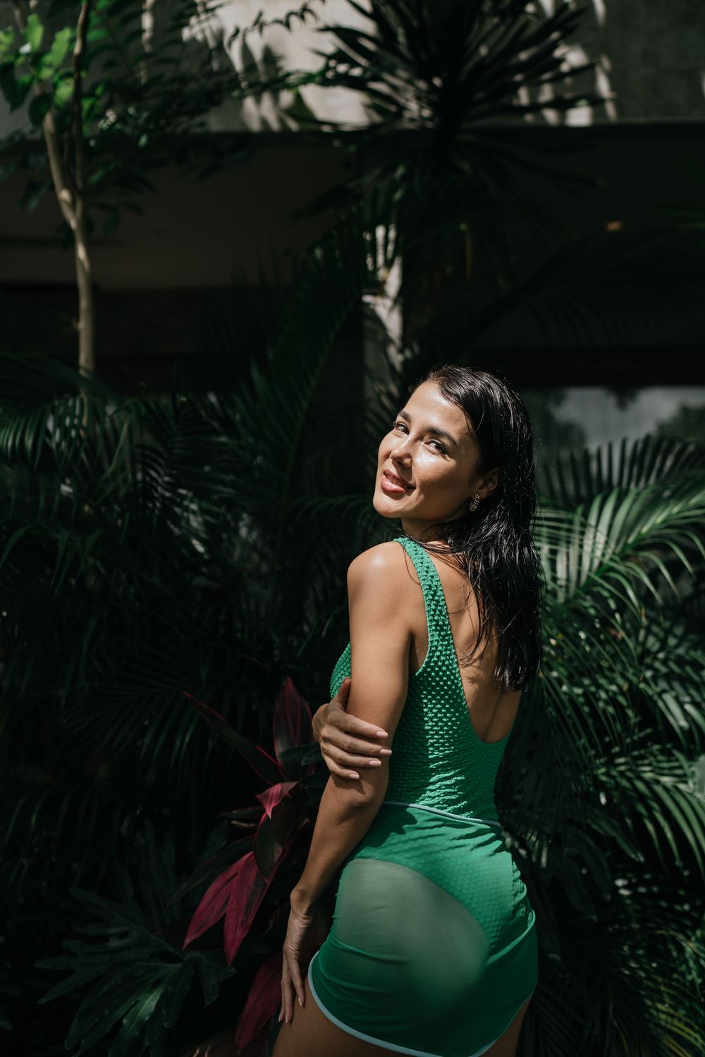 Artistic portrait of woman in emerald swimsuit among tropical plants.