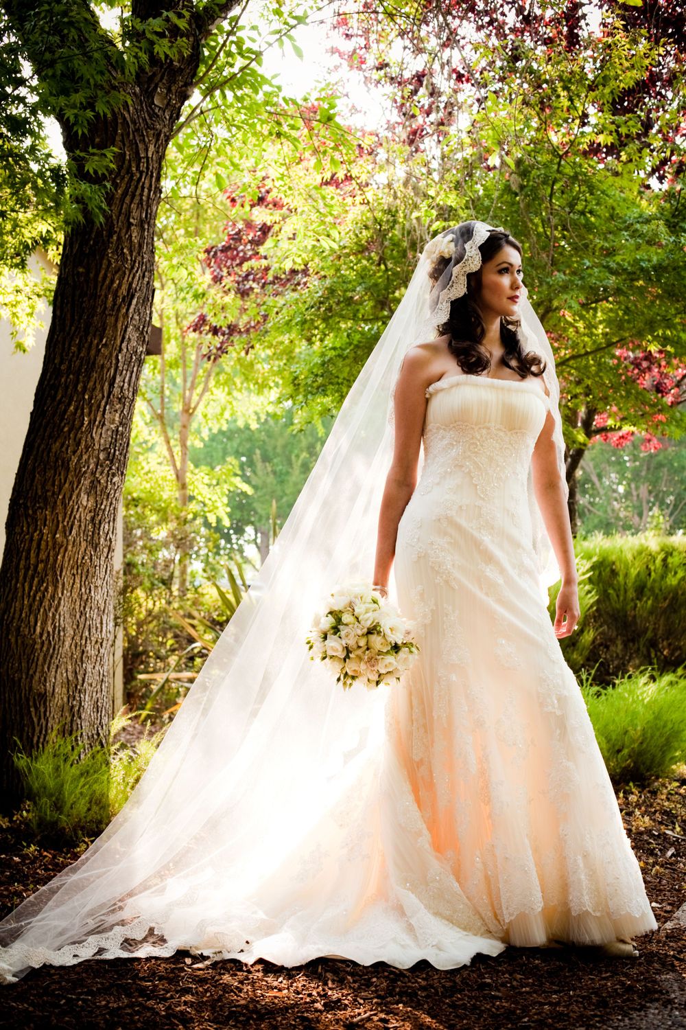 Full-length bridal portrait in garden setting with flowing white gown and bouquet.