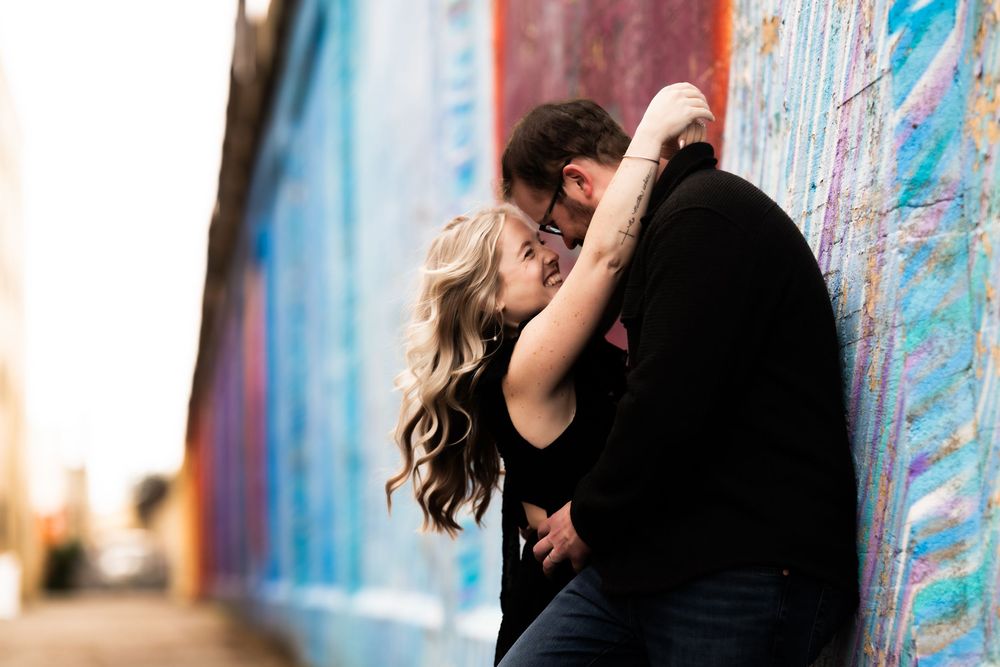 A couple in black clothing dances together against a colorful graffiti wall backdrop.