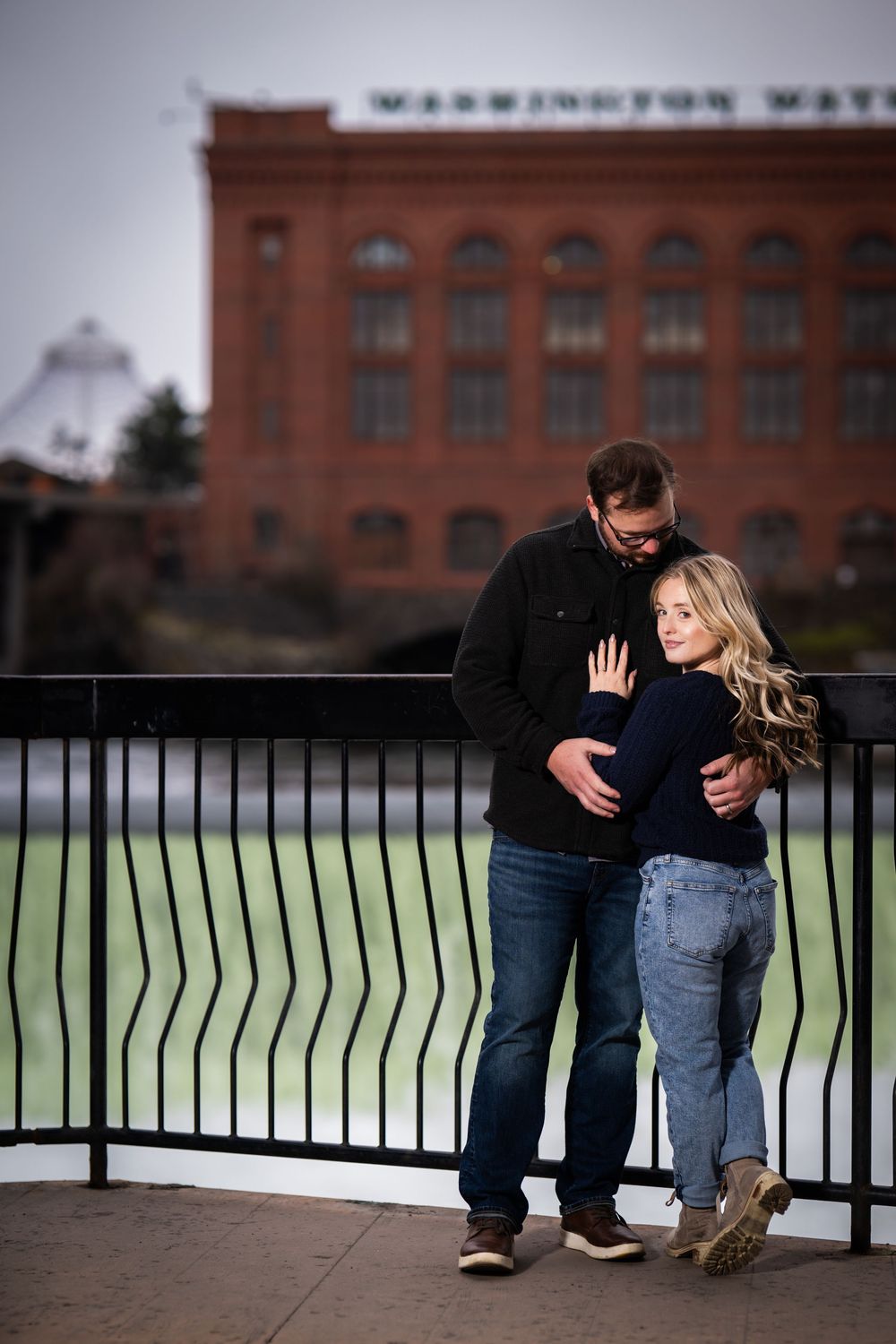 Couple sharing an intimate moment along an urban railing with brick buildings in the background.
