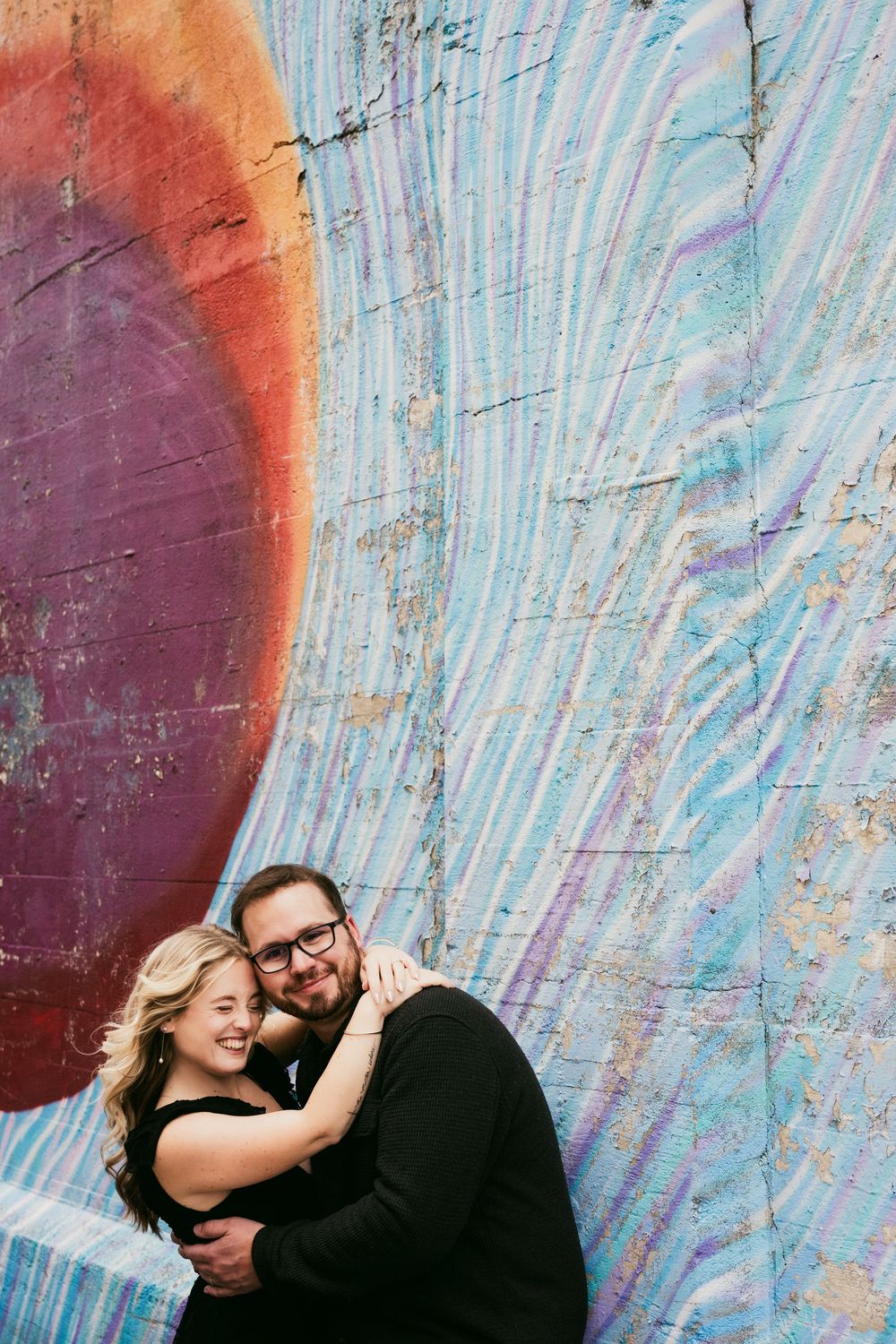 A couple shares a romantic moment against a colorful abstract painted wall background.