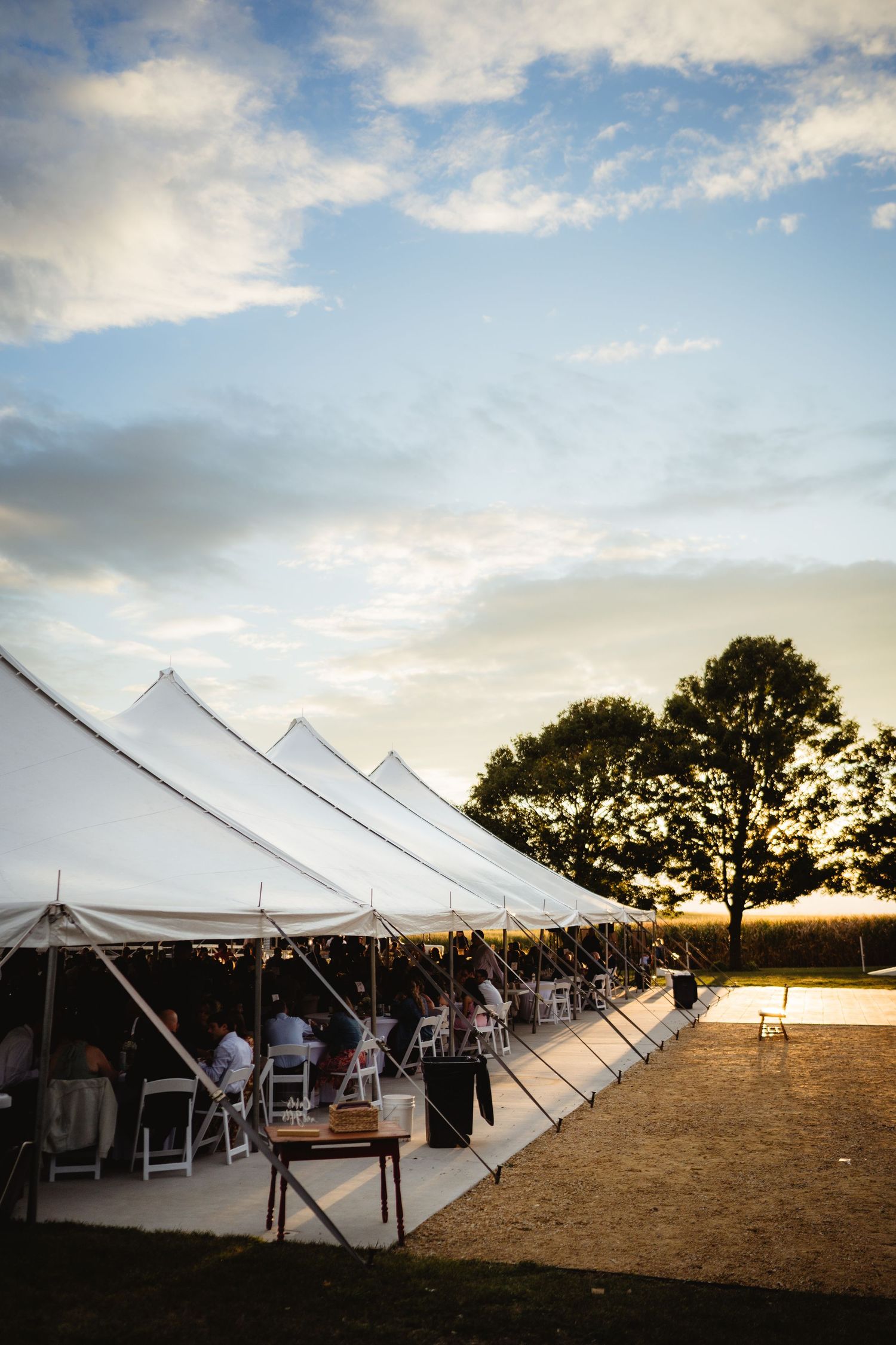 A series of white wedding tents at sunset on a beach with golden light and cloudy skies.