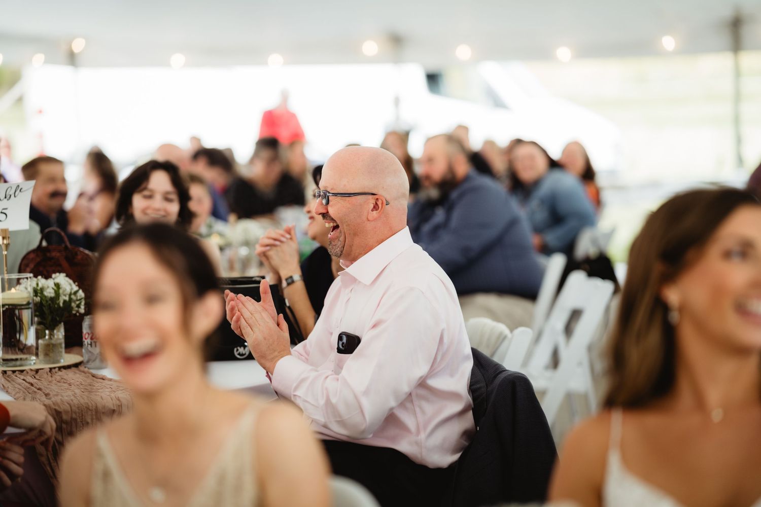 Event guests listen attentively during a presentation in a white tent venue with natural lighting.