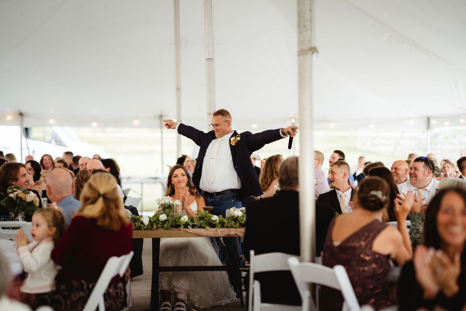 Wedding reception guests dancing and enjoying themselves under a white tent at an outdoor celebration.