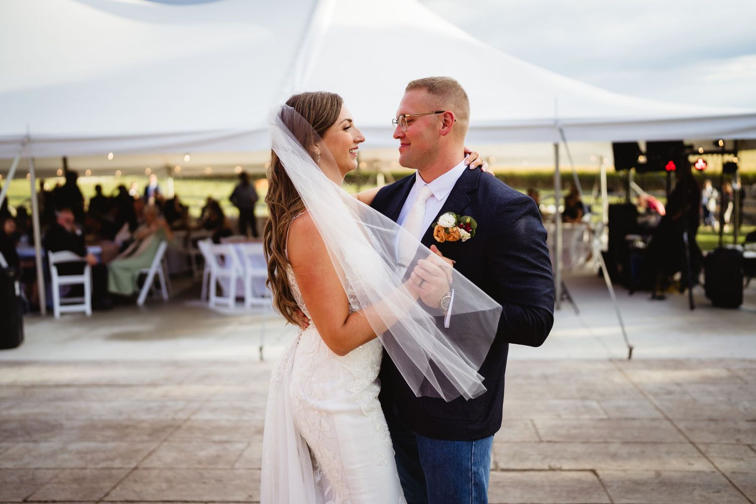 A couple shares their first dance as newlyweds under an elegant white tent during an outdoor wedding reception.