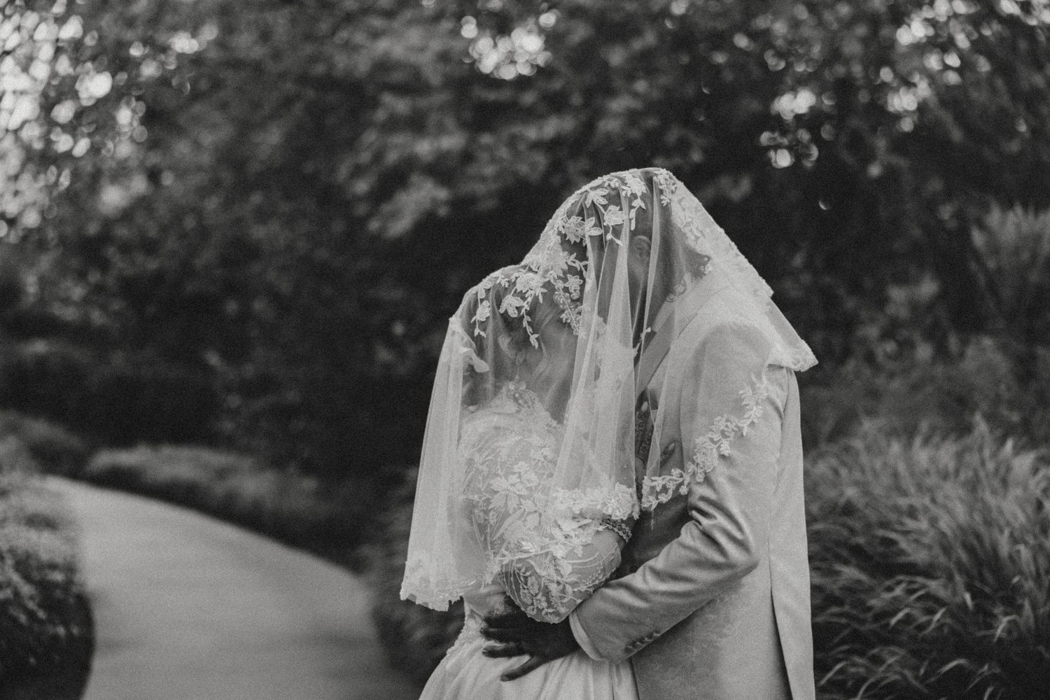 A romantic black and white photo series of a couple walking along a garden path in wedding attire.