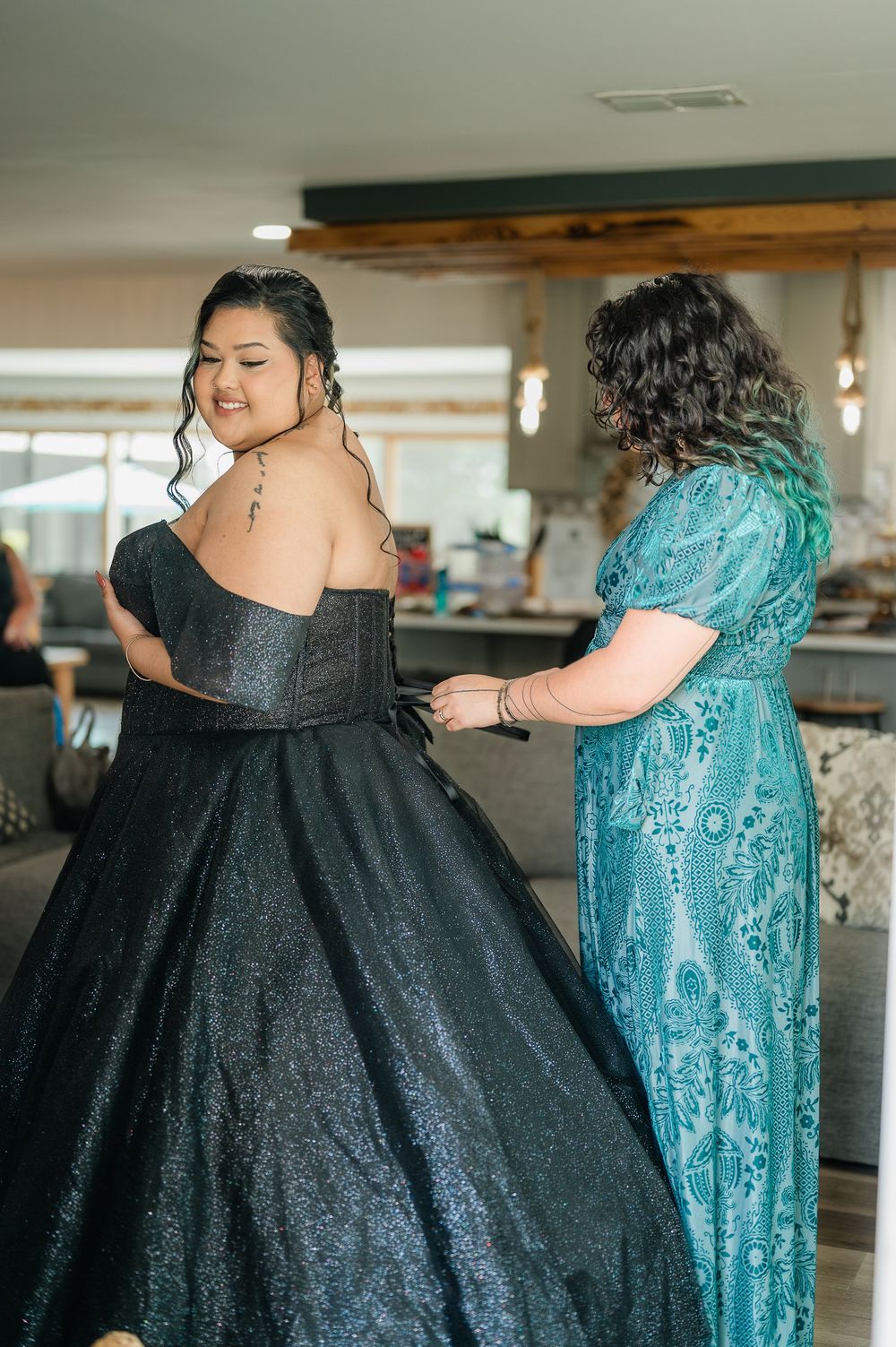 Wedding party members embrace while wearing elegant teal and black formal dresses.