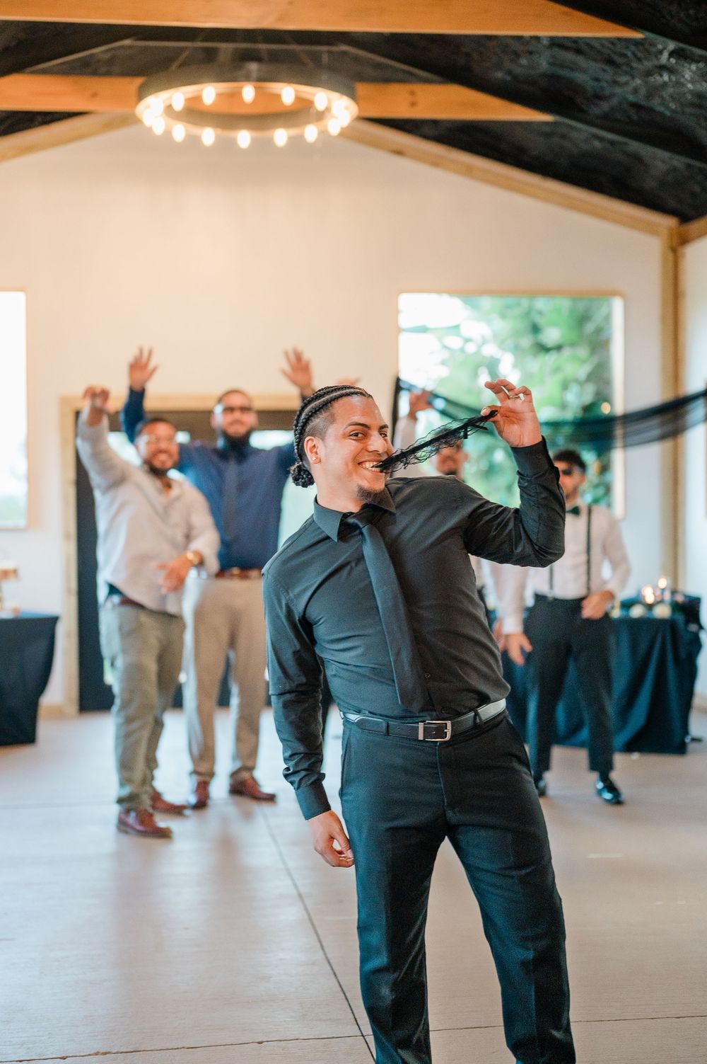 Wedding party members dancing with raised hands in celebration at an indoor reception venue.
