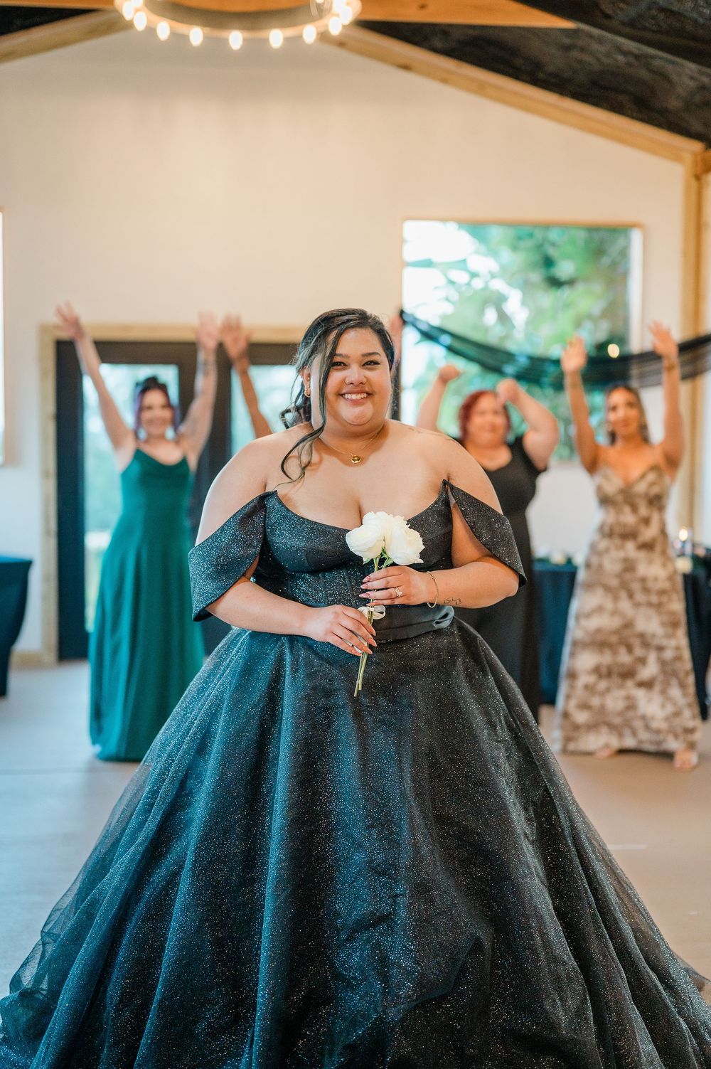 A woman in a stunning black ball gown stands in celebration at a wedding reception with guests in formal attire.