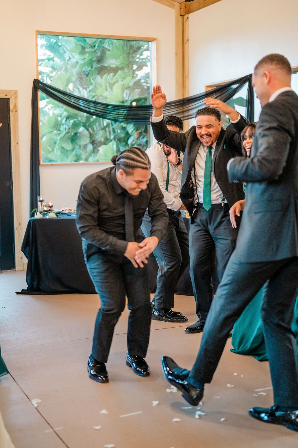 Groomsmen perform a fun choreographed dance sequence in formal black suits at a wedding reception.