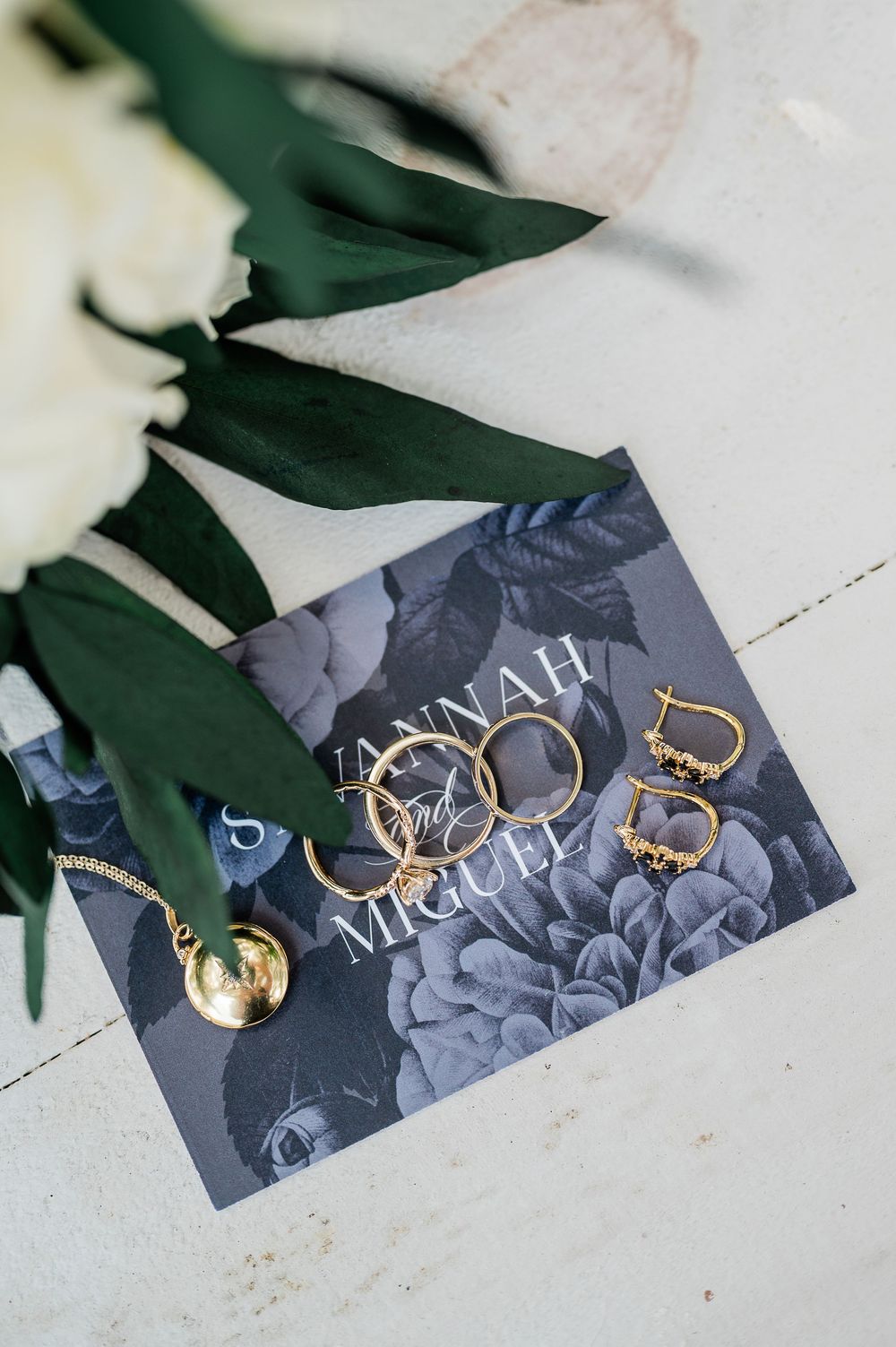 Wedding rings and jewelry displayed on an elegant gray floral business card.