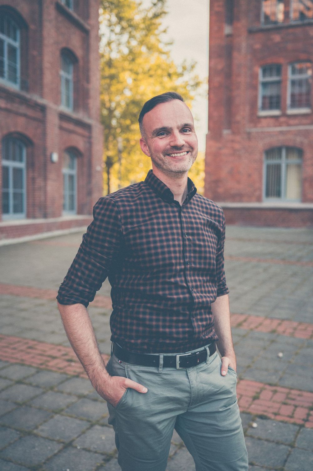 Three similar photos of someone wearing a plaid shirt and gray pants standing outdoors near brick buildings in autumn.