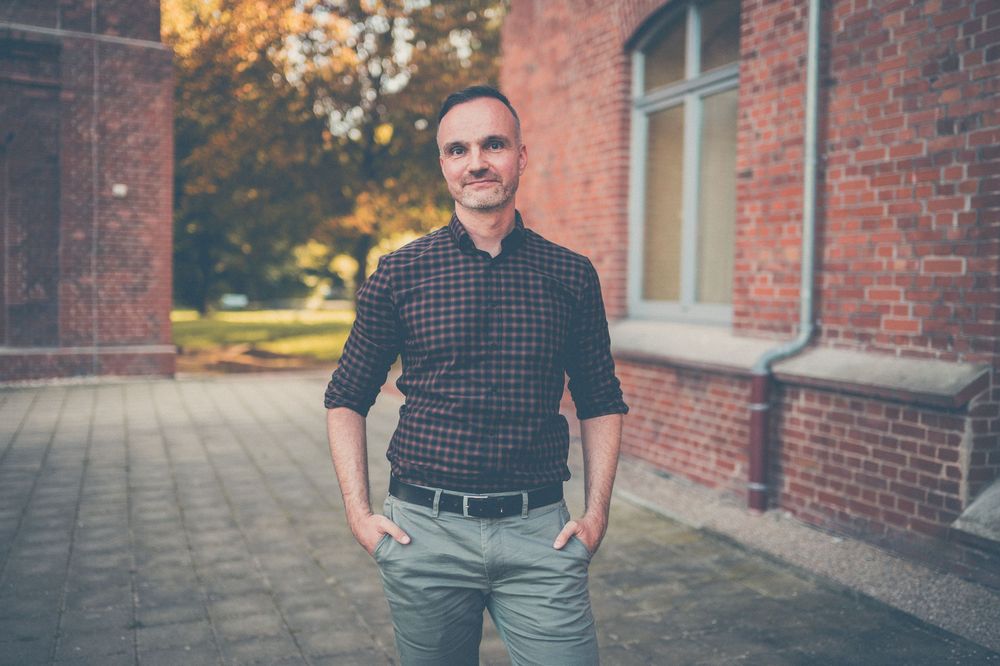 Professional standing outside brick building in casual attire during autumn season.