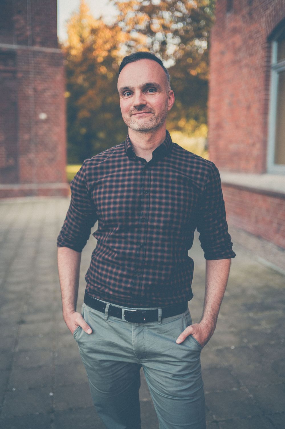 A series of casual portrait shots against a brick wall showing someone wearing a plaid shirt and gray pants.
