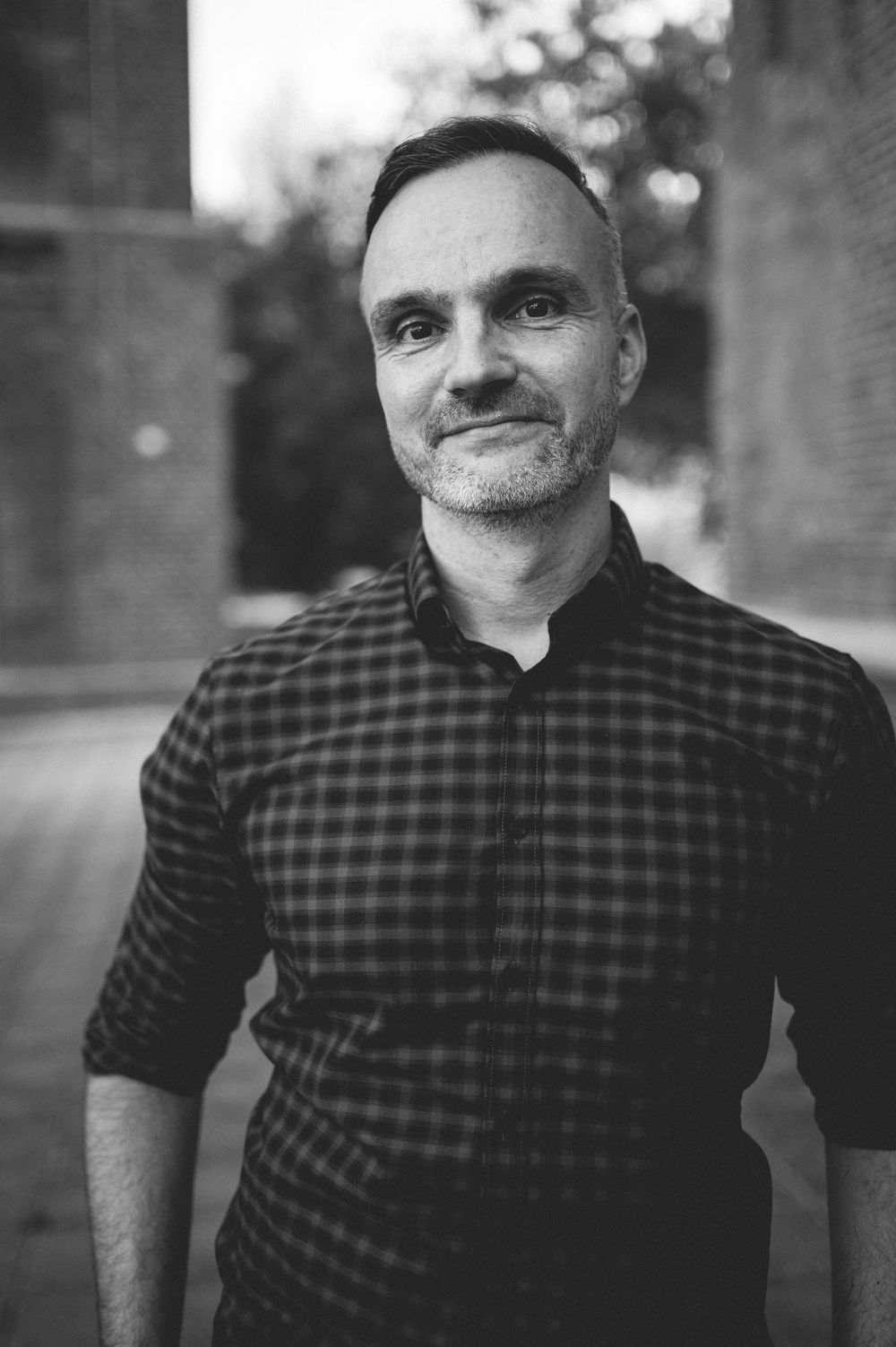A black and white portrait series showing someone in a plaid shirt smiling and posing against a blurred background.