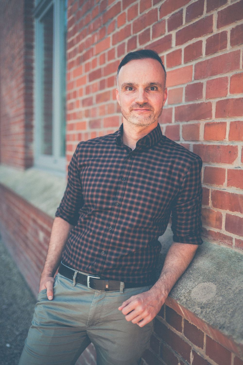 Several photos of a casual look with plaid button-down and gray slacks against red brick background.