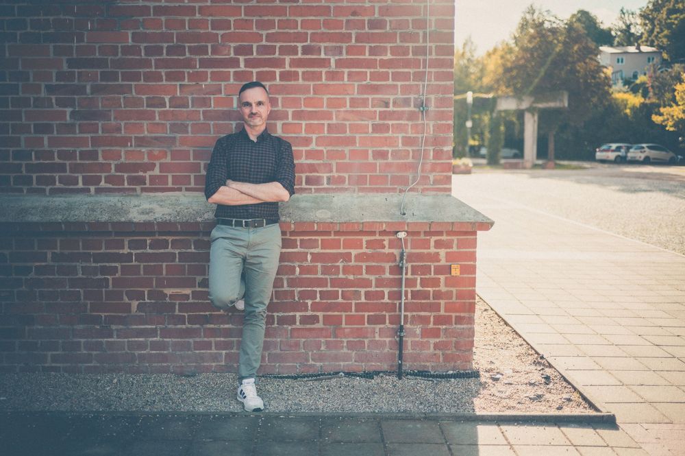 Someone leans casually against a brick wall wearing casual attire on a sunny afternoon.