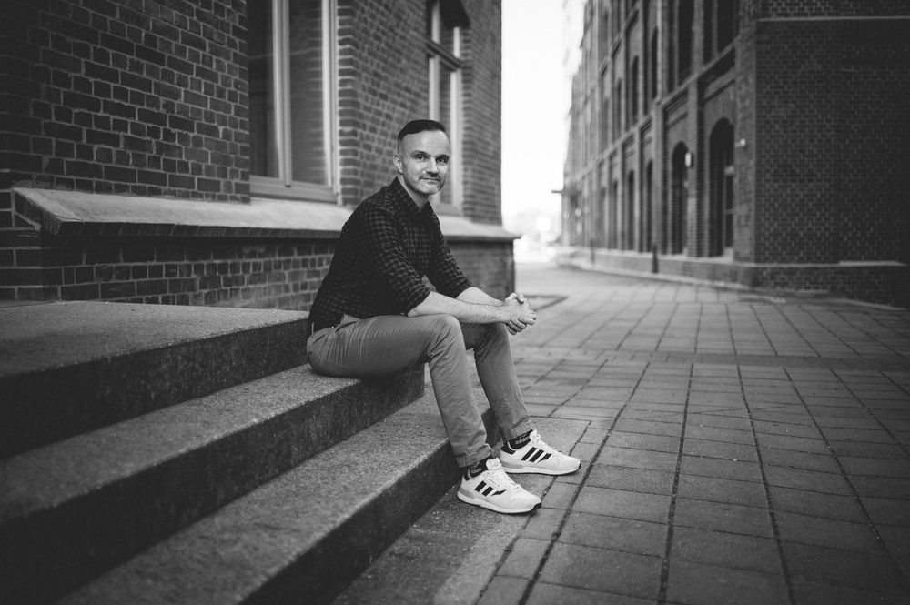 Black and white photo of someone sitting on brick building steps wearing sneakers along an urban street.