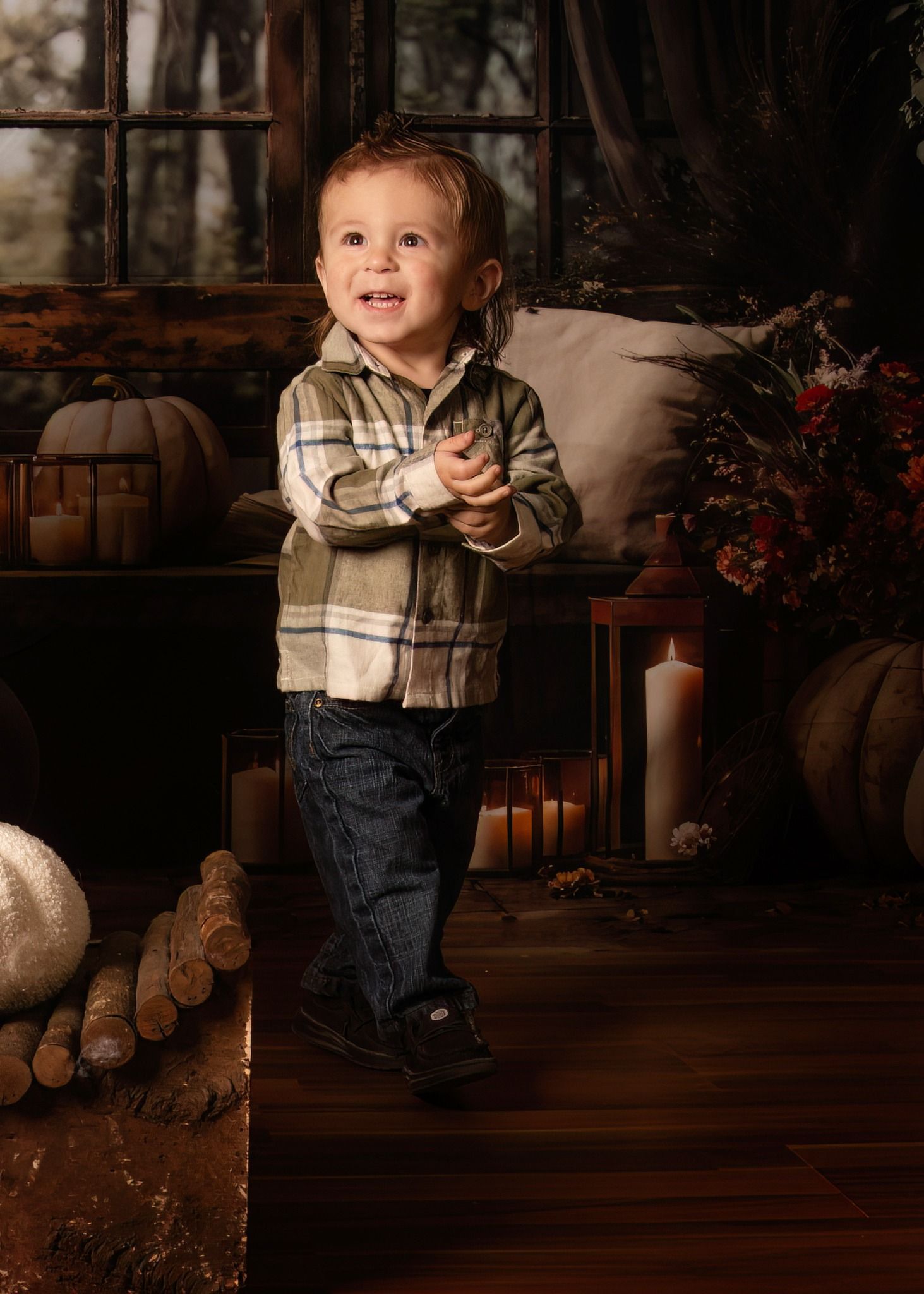 A toddler wearing a plaid shirt and jeans stands on a hardwood floor in a rustic, warmly lit indoor setting.