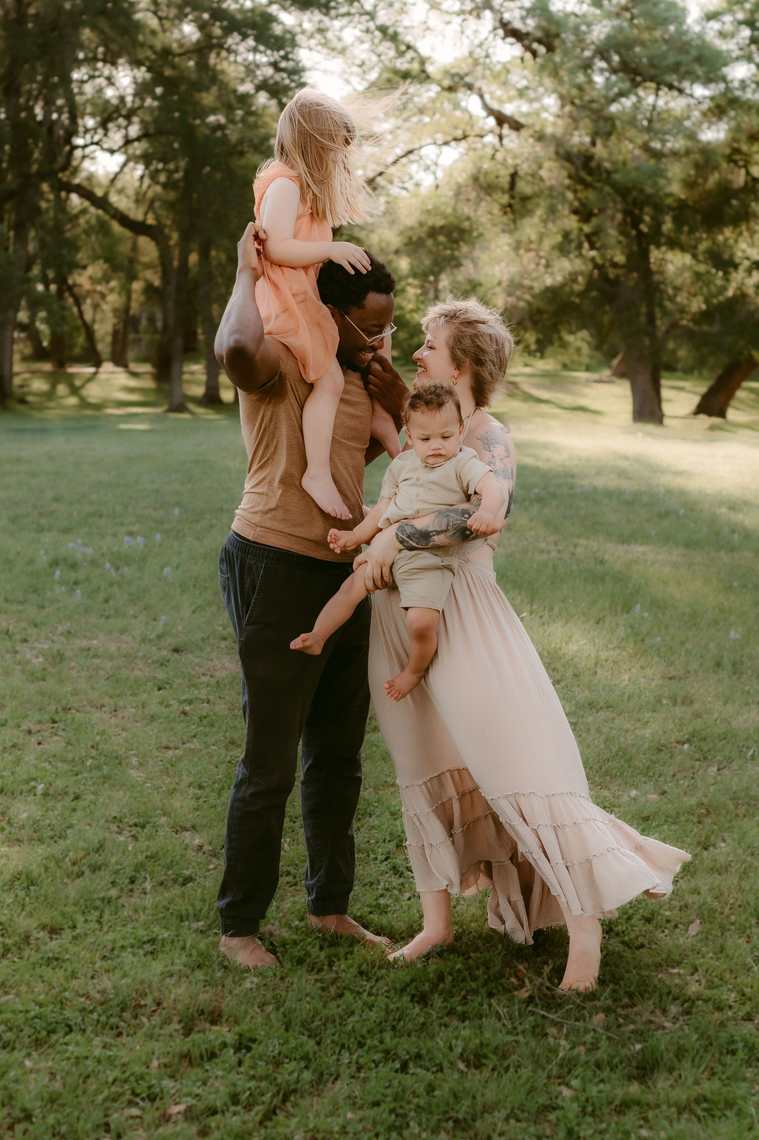 A family shares tender moments together while dancing and embracing on grassy parkland at sunset.
