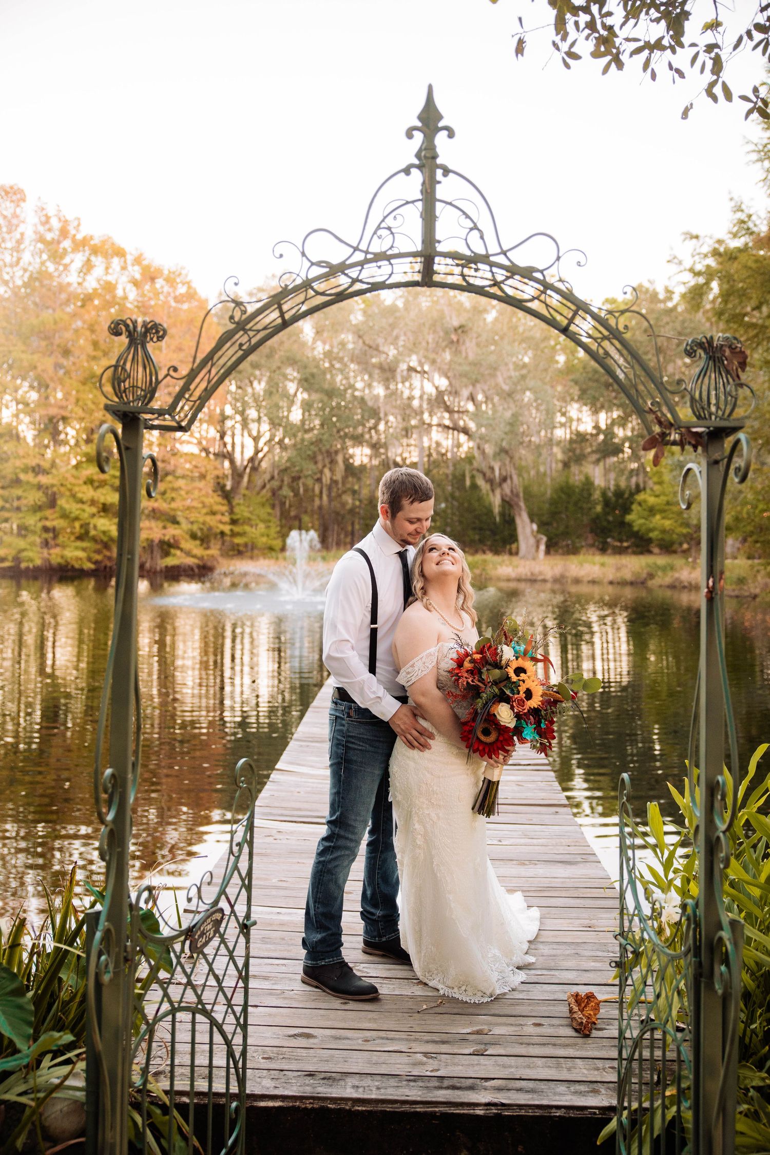Wedding photos of a couple on a wooden dock with ornate railings overlooking a peaceful lake at sunset.