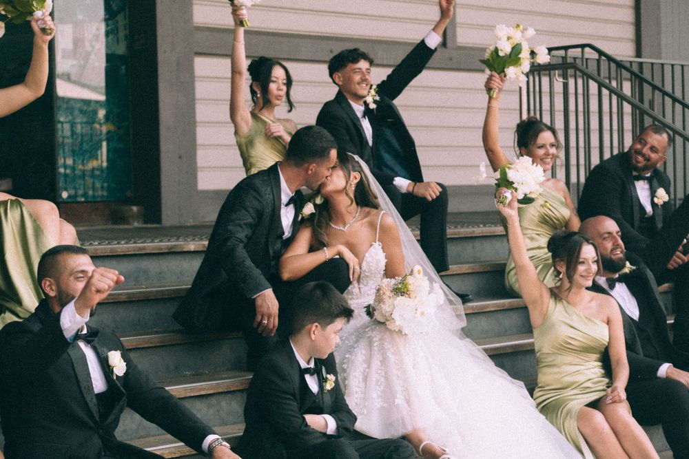 Wedding party members celebrating on elegant stone steps with joyful expressions and formal attire.