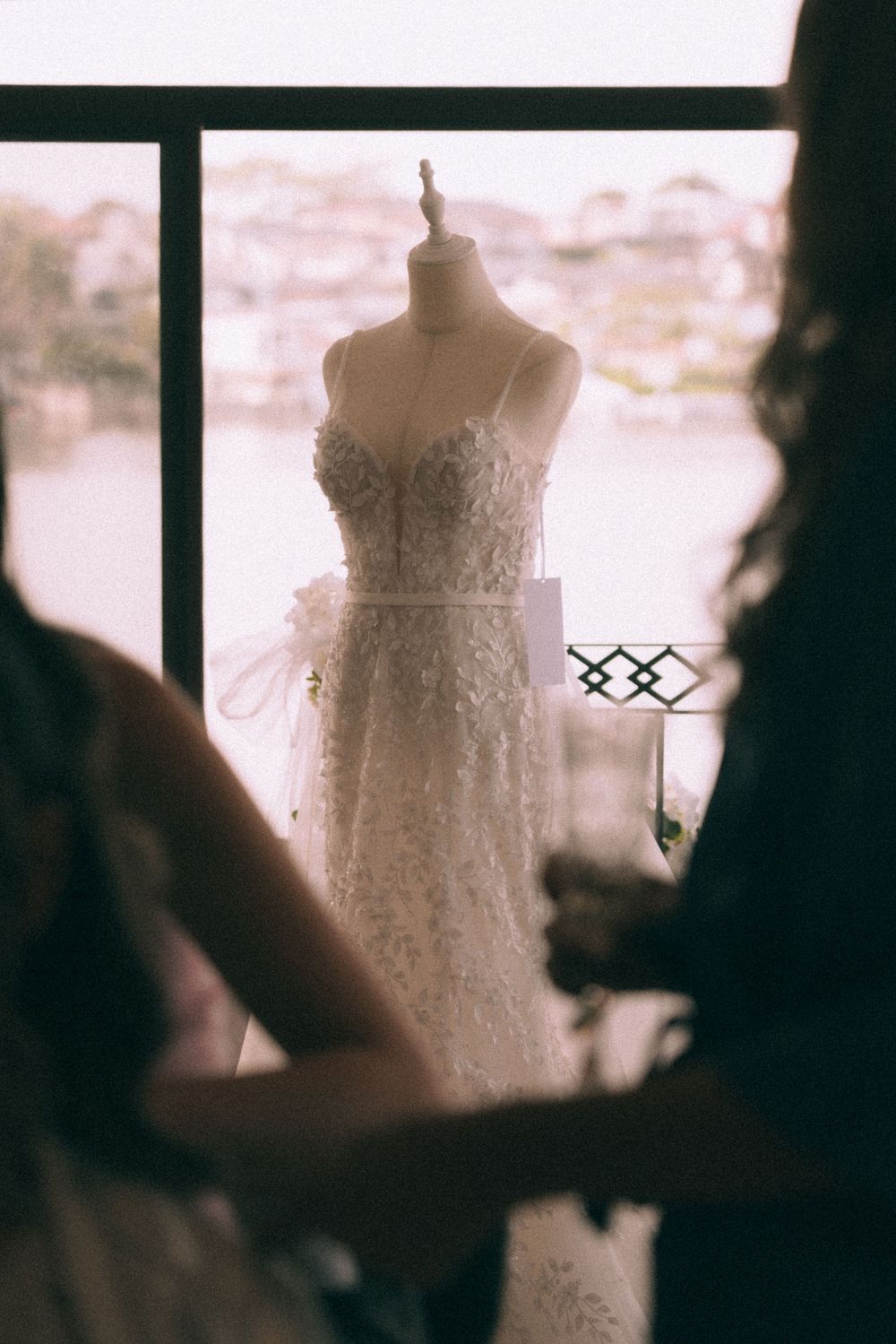 A delicate white lace wedding dress on a mannequin form displayed by a window in soft natural light.