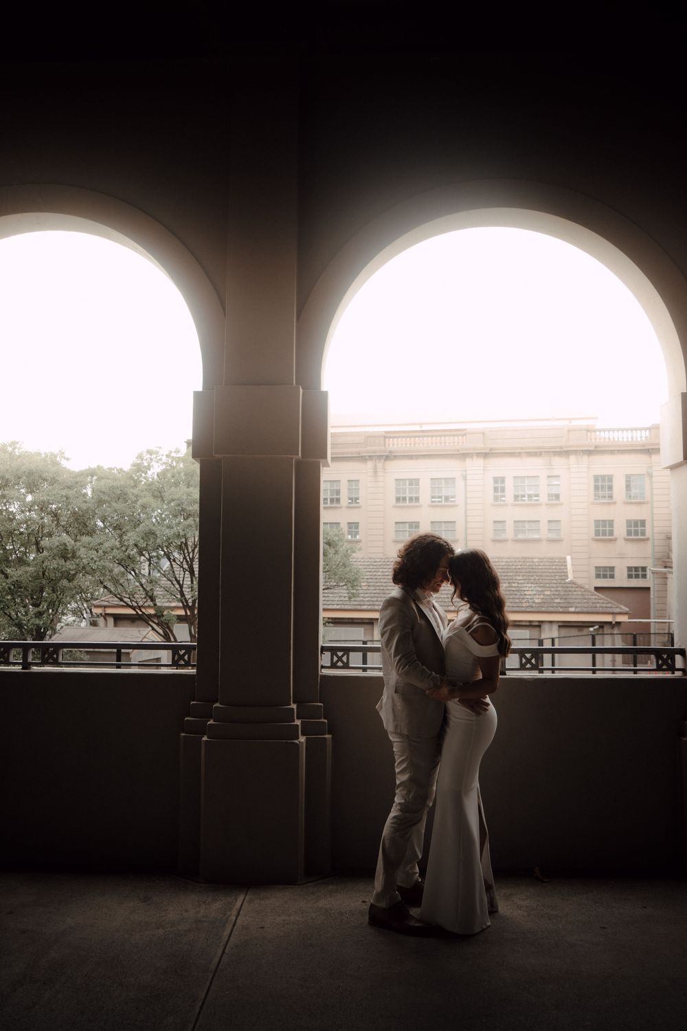 A romantic silhouetted couple shares an intimate moment under an archway casting dramatic shadows and light.