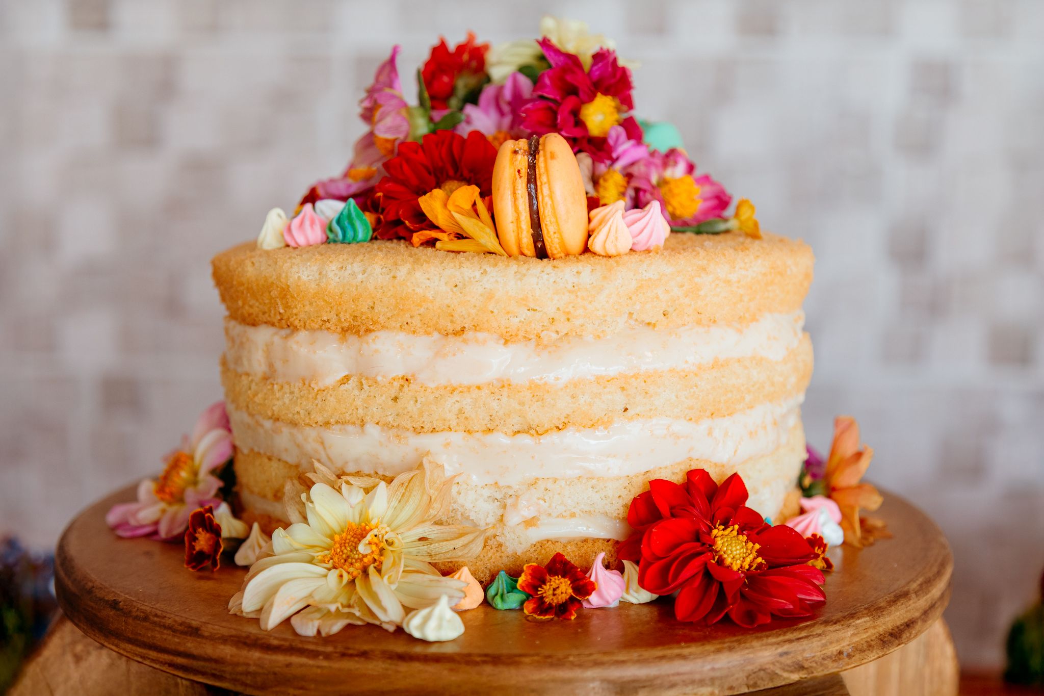 Seven decorative layer cakes adorned with colorful fresh flowers and berries sit in a row on wooden cake stands.