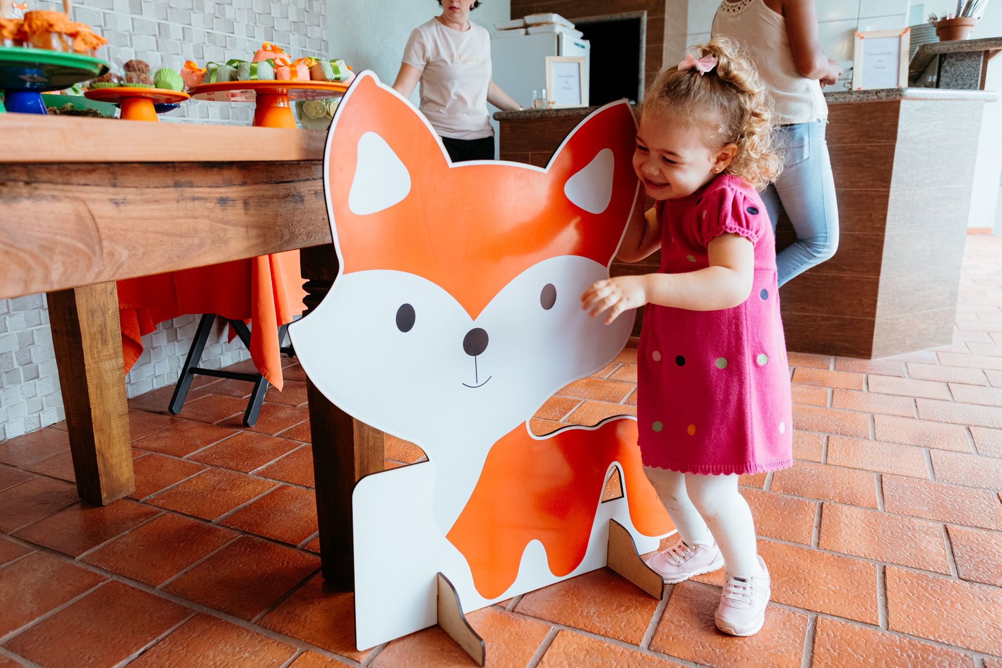 A person in a pink dress stands next to a large decorative fox cutout on a terra cotta floor.