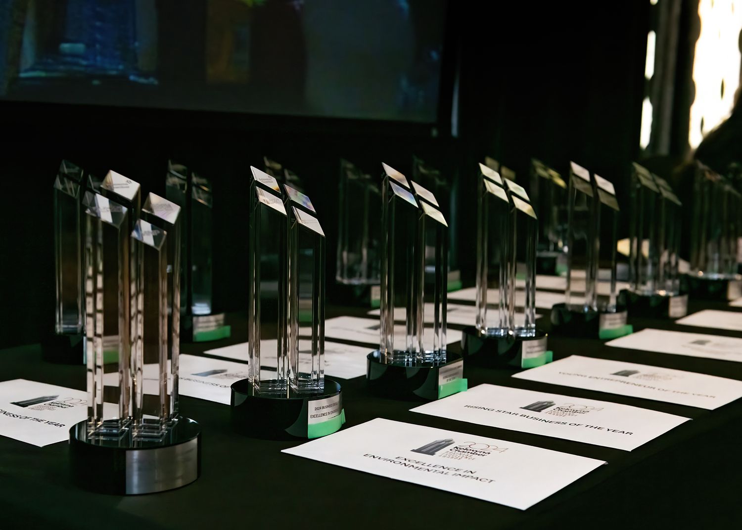 Row of glass awards trophies displayed on a table with name cards in front.