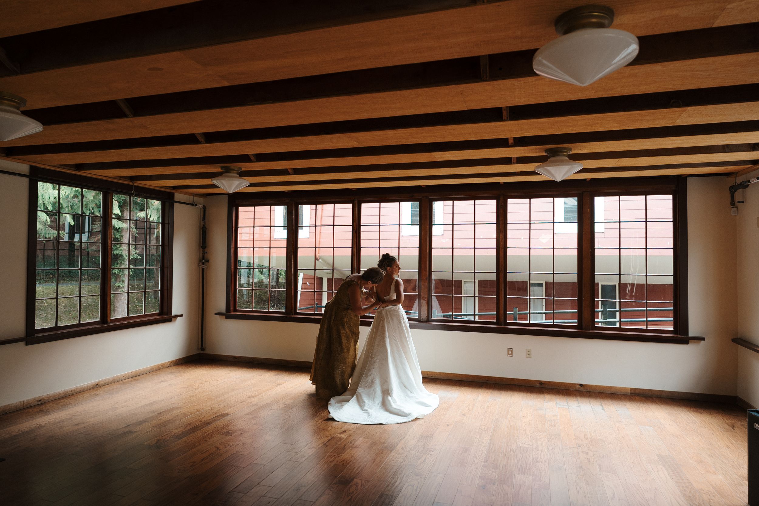Bride and groom share intimate first dance in rustic wooden venue with large windows and warm hardwood floors.
