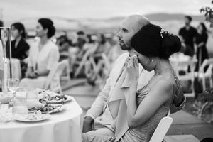 Wedding guests enjoy an elegant dinner reception at tables decorated with white linens and floral centerpieces.