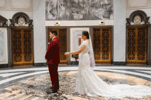 Two people in formal attire walk together on a patterned marble floor in an elegant building interior.