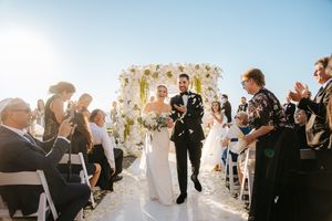 Wedding guests celebrate with bubbles as newlyweds walk down outdoor aisle during sunset ceremony.