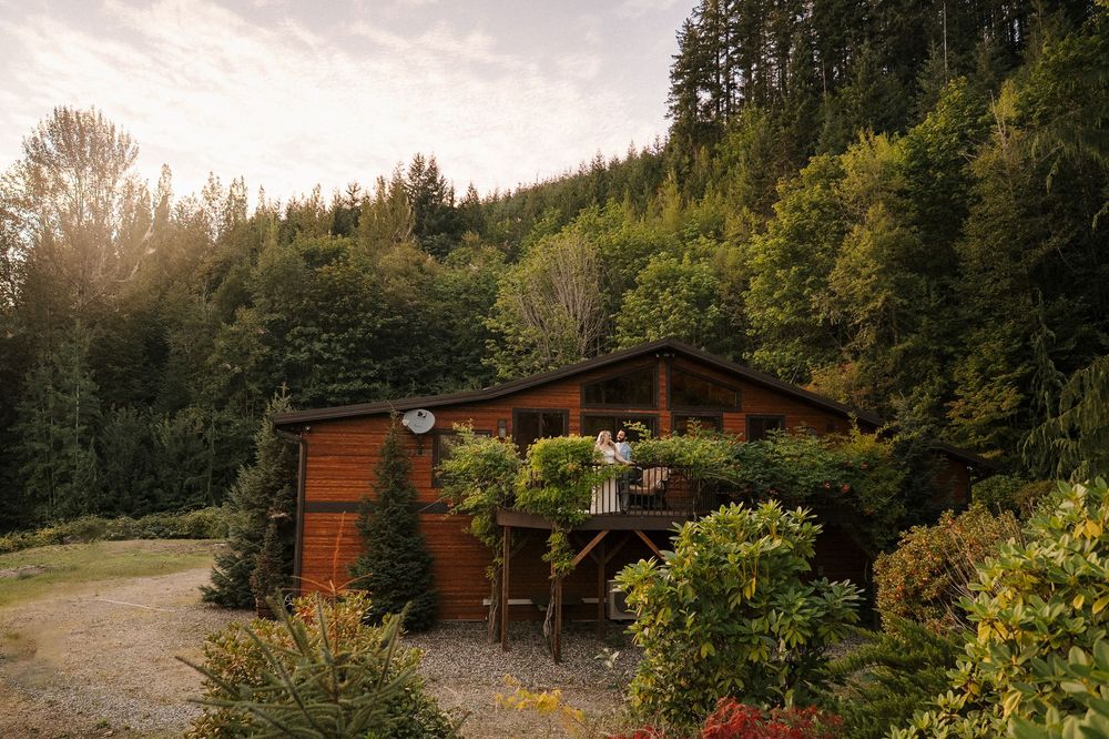 Rustic wooden cabin nestled in a lush forest setting with sunlight peeking through trees at dusk.