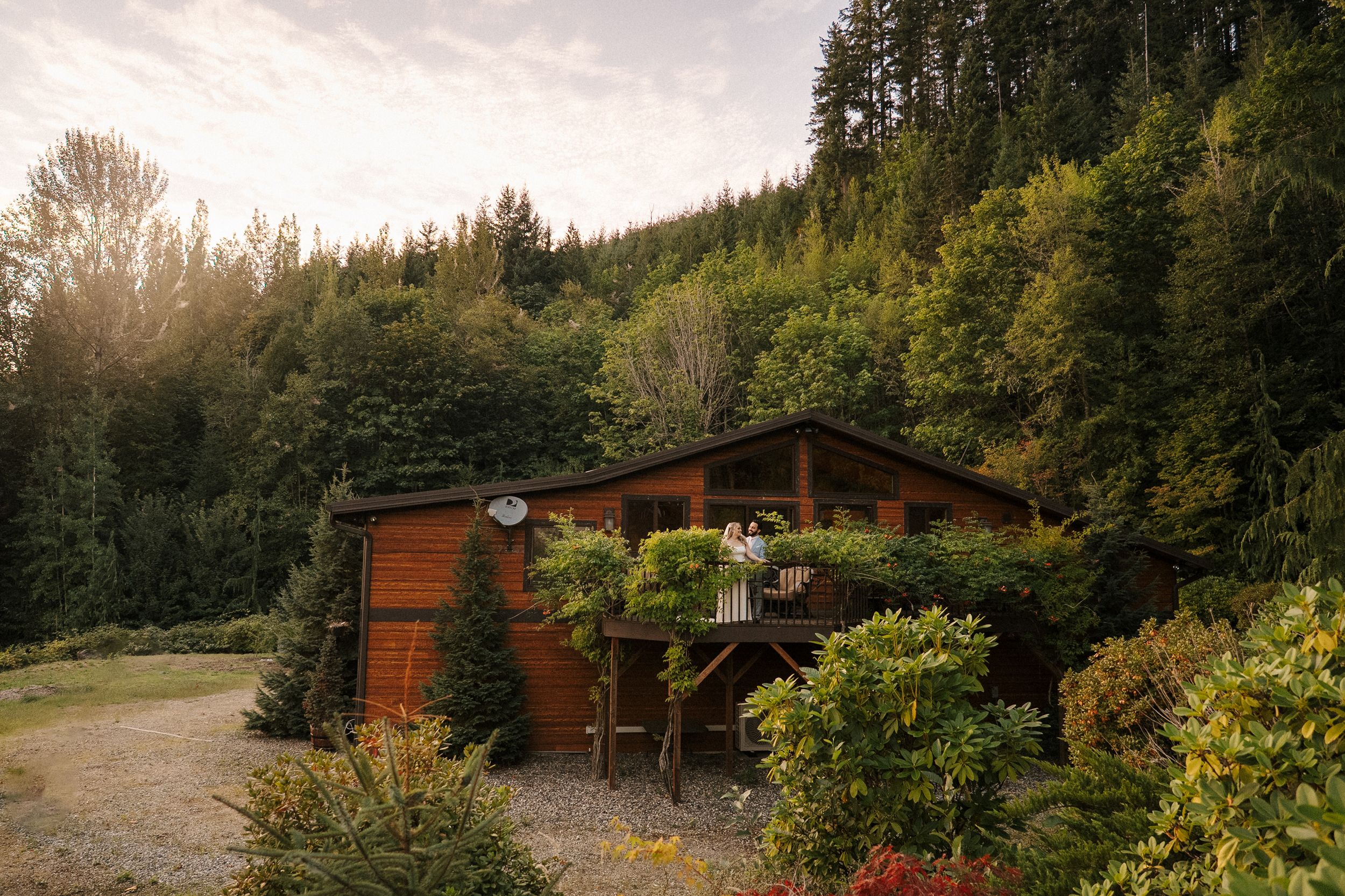 Rustic wooden cabin nestled in a lush forest setting with sunlight peeking through trees at dusk.