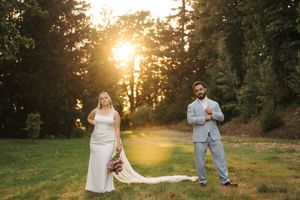 A couple shares a romantic moment in a sunlit meadow during golden hour as the sun sets behind tall trees.