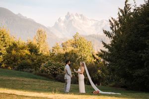 Couple walking through a golden sunlit field at sunset with mountains in the background.