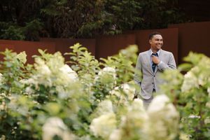 A wedding couple walks through a garden pathway with white hydrangea flowers blooming in the foreground.