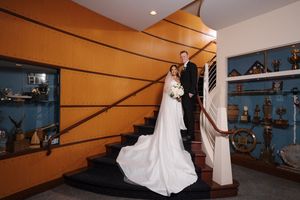 A person in a flowing white wedding dress stands on stairs against an orange wall with blue shelving displaying decorative items.