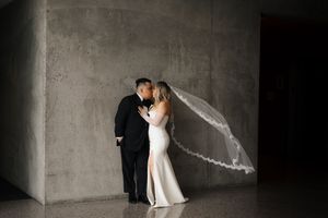 A bride and groom embrace in an industrial concrete space as her veil flows behind them.