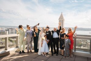 Wedding party poses together on a waterfront deck overlooking a scenic harbor view during a celebration.