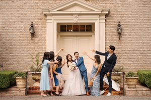 Wedding party members gather on stone steps outside a historic brick building for candid photos.