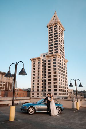 Classic car parked in front of an art deco style high-rise building with vintage street lamps at dusk.