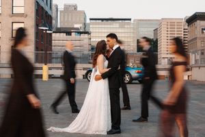 Wedding party in formal attire stands in line on an urban rooftop at sunset.