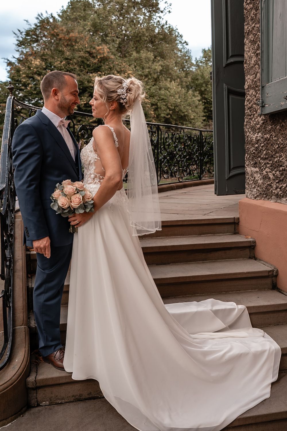 Couple in wedding attire sharing an intimate moment on outdoor steps with flowing white dress and veil.
