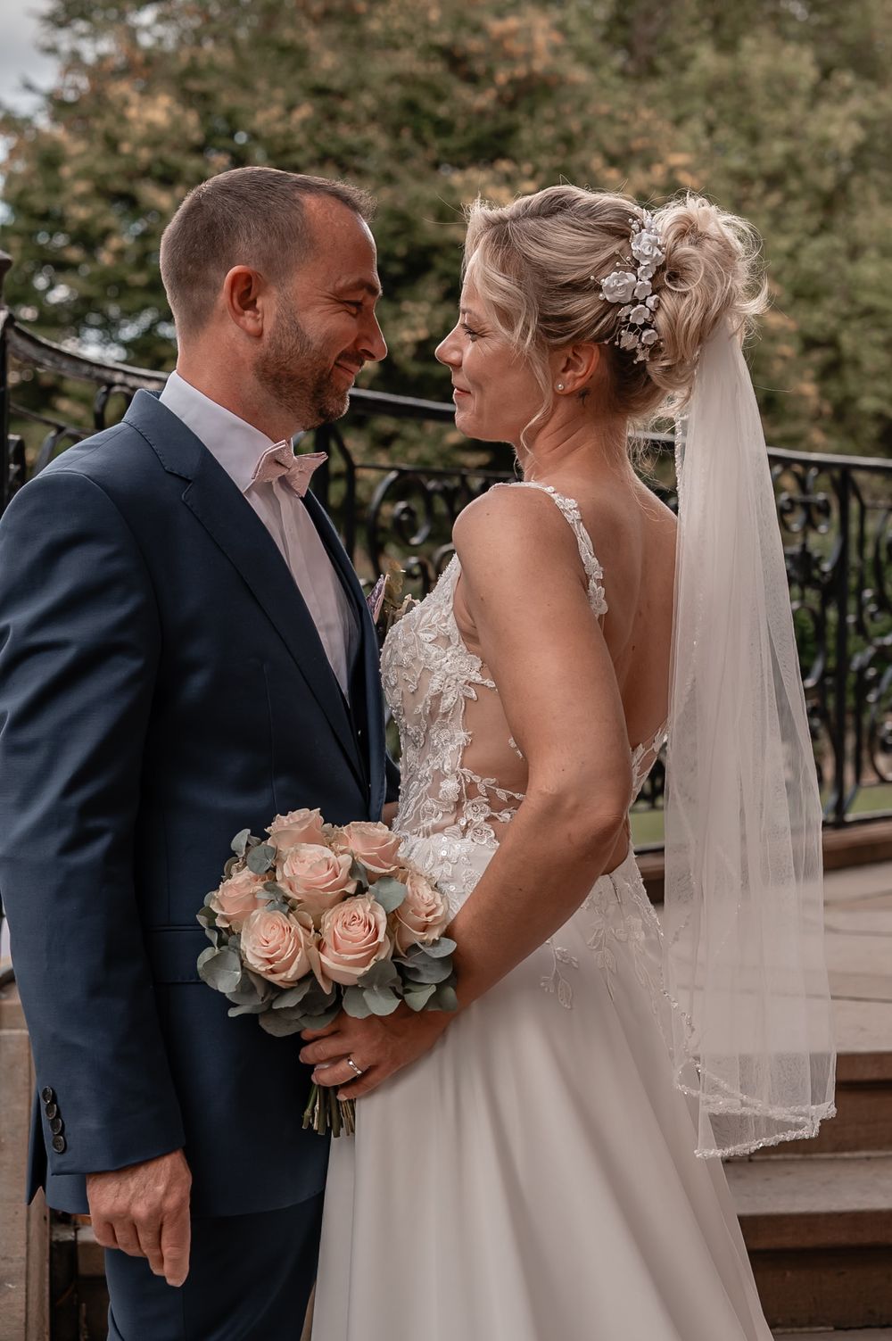 A romantic wedding moment captured outdoors with the bride holding a bouquet of peach roses.